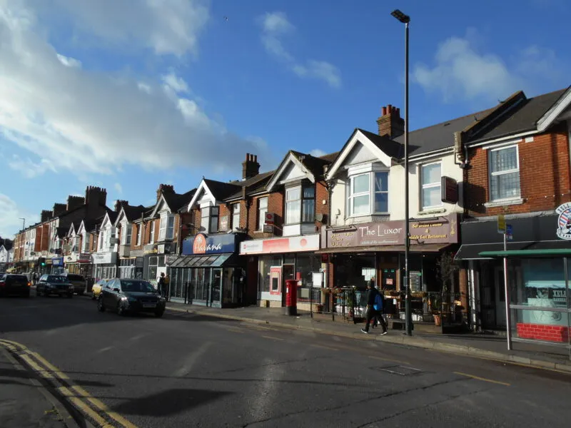 Shops and restaurants along a sunny stretch of Charminster high street, with a red postbox on the pavement