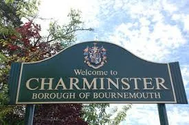 Green road sign reading 'Welcome to Charminster, Borough of Bournemouth' with a coat of arms