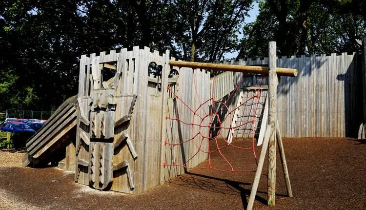 Wooden fort-style climbing frame with a slide and a red rope net in a children's play area