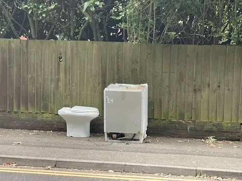 Fly-tipped fridge and toilet left on a pavement beside a wooden fence