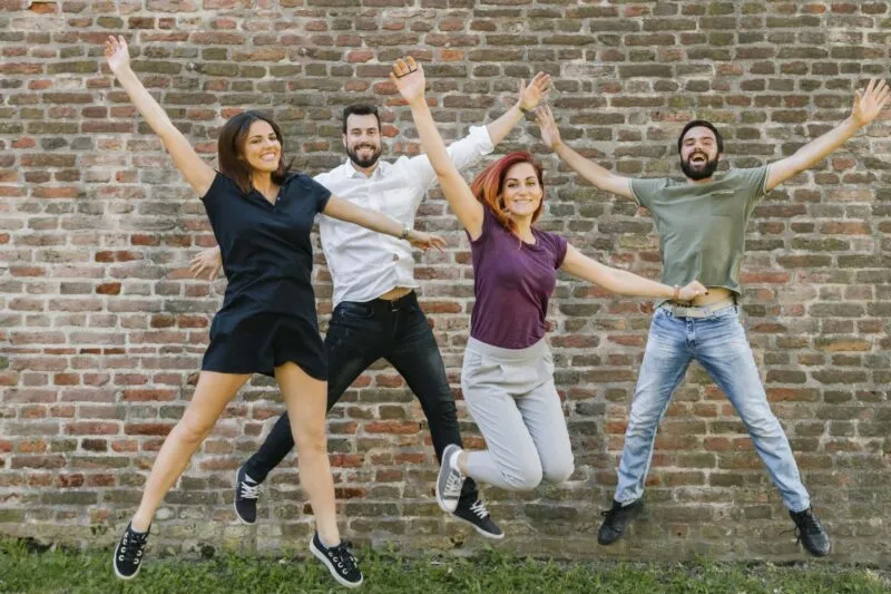 Four smiling friends jumping in front of a brick wall