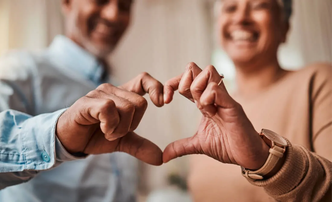 Two smiling people joining their hands to make a heart shape