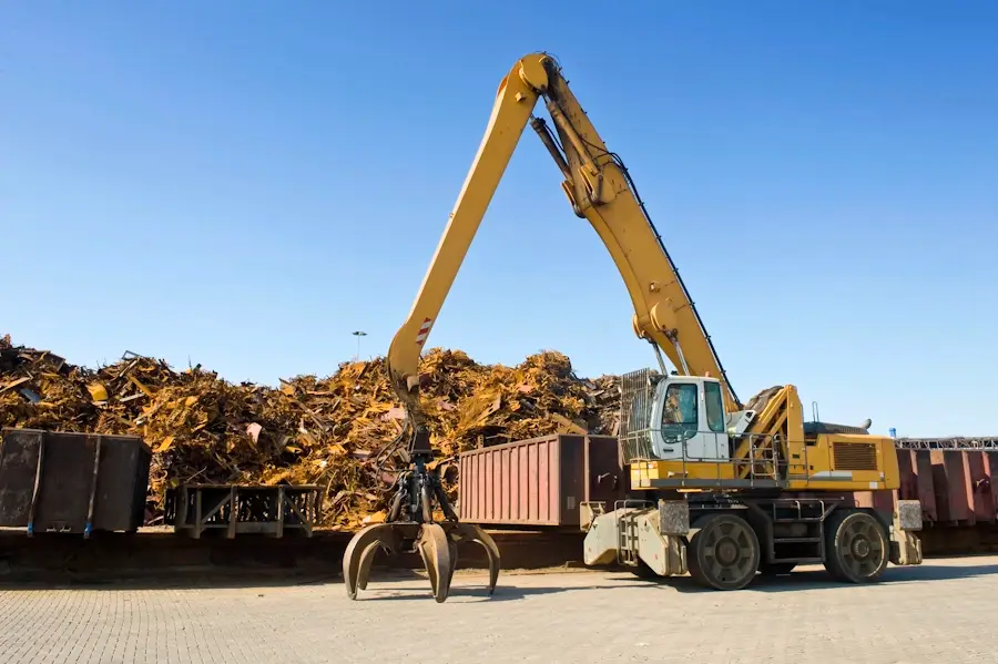 Yellow grab excavator beside a large heap of scrap metal at a waste site